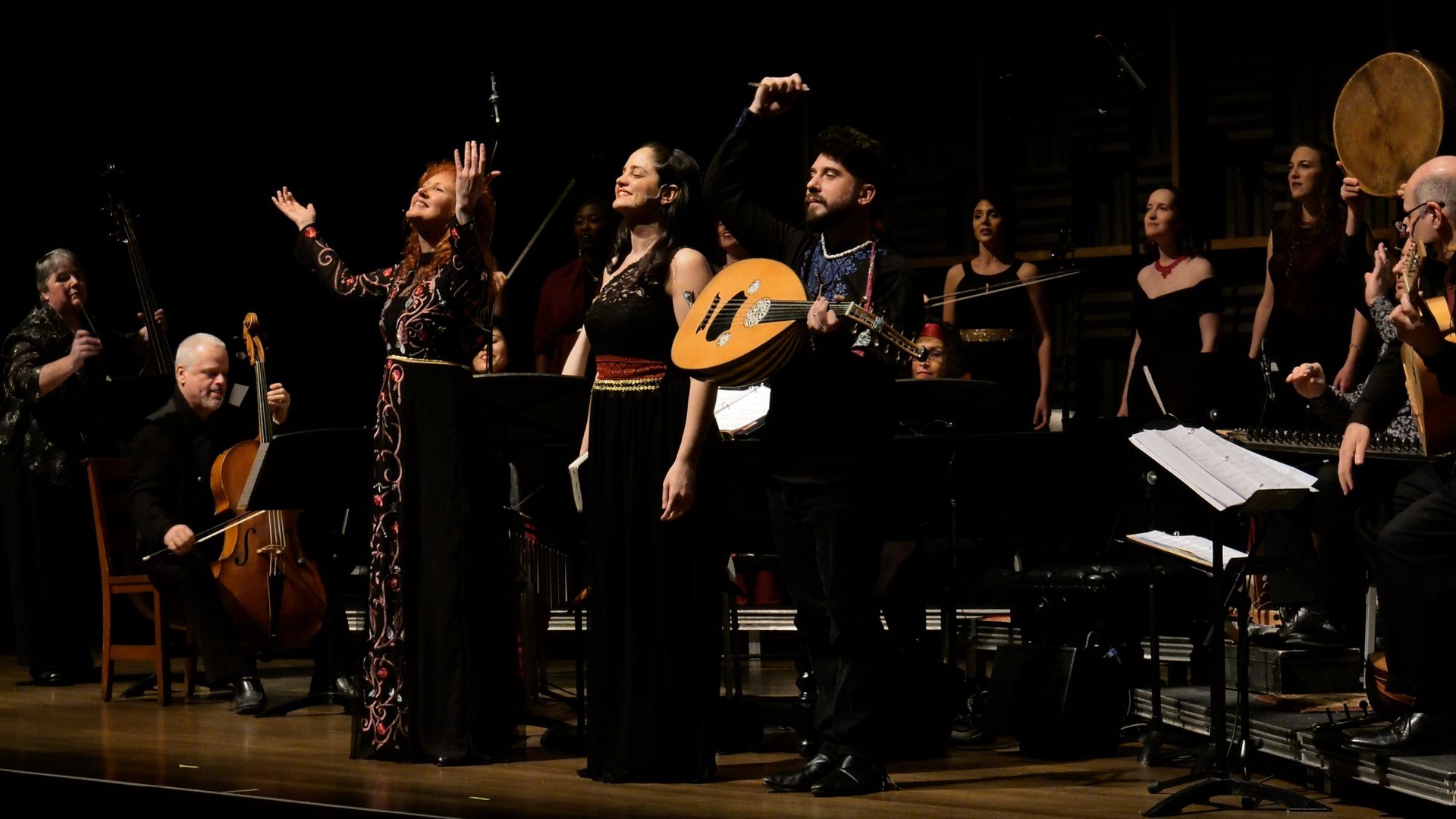 Three musicians who have just finished performing stand in front of an ensemble of other musicians.